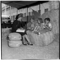 Mrs. Rosita Yacopi writes with three young children sitting on a hay bale at the Shrine Charity Circus, Los Angeles, June 1946