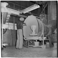Employee sprays a ceramic toilet bowl with a hose at the Universal Vitreous China Factory, Mentone, circa 1948