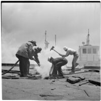 Fire fighters using an axe and a hose on a marine terminal in L.A. Harbor to fight at fire caused by the Markay oil tanker explosion, Los Angeles, 1947