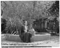 Avila Adobe, view of patio with fountain and seated woman with watering can, Olvera Street, Los Angeles, 1934