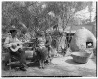 Avila Adobe, view of patio with woman and man with guitar seated on bench, Olvera Street, Los Angeles, 1934
