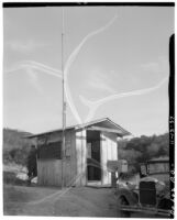 Unidentified man leans on small post office building, De Luz, 1937