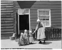 Three little girls and a woman wearing traditional Dutch clothing outside a house, Holland, 1929