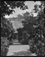 Gardens at Alcázar of Seville, view down a walkway towards a courtyard with a high wall, Seville, Spain, 1929
