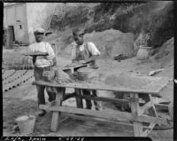 Two men making clay roofing tiles at a picnic table in Loja, Spain, 1929