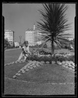 Carolyn Bartett seated on lawn and admiring flowers in the garden at the Municipal Auditorium, Long Beach, 1932