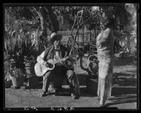 Eugene R. Plummer with guitar and Indian artifacts, with woman in shawl, West Hollywood, 1927