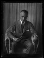 Portrait of Adelbert Bartlett, in suit and tie, seated in wicker chair in front of curtain, [1923?]
