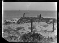 Man seated on rock wall at the beach, Malibu, 1929