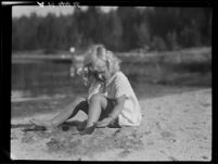 Girl playing with sand on lakeshore, Lake Arrowhead, 1929