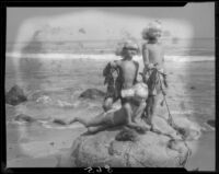 Mawby triplets on rock with seaweed at beach, Malibu, 1928