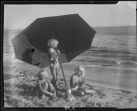 Mawby triplets with umbrella and dolls at beach, Malibu, 1928
