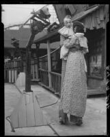 Clown on stilts dancing with tall puppet, advertising dance marathon, Santa Monica, 1928