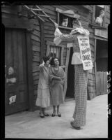Clown on stilts, advertising dance marathon, facing two women, Santa Monica, 1928