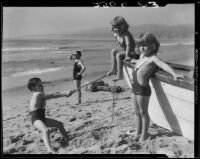 Patsy, Peggy, and Tommy Morgan playing on beach with boat and rope, Santa Monica, 1929