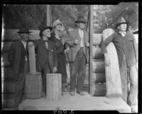 Men and woman posing with log cabin under construction, San Bernardino, 1925-1928