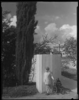 Adelaide Rearden posing with a tricycle next to a cypress tree, Santa Monica, circa 1928