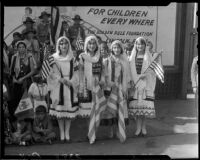 Group in Greek ethnic dress posing with billboard advertising Golden Rule Week at Golden Rule Foundation Pageant, Los Angeles, 1930