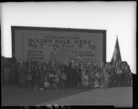 William Gibbs McAdoo, John Willis Baer, and group posing with billboard advertising Golden Rule Week at Golden Rule Foundation Pageant, Los Angeles, 1930