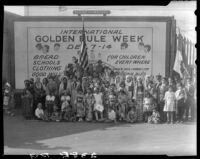 Children in ethnic dress posing with billboard advertising Golden Rule Week at Golden Rule Foundation Pageant, Los Angeles, 1930