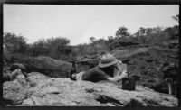 Paul Rotha on the bank of the Victoria Nile River lying looking through a camera during a journey to Murchison Falls, Uganda, 1933