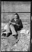 Filmmaker Paul Rotha leaning on wall reading newspaper, Engand, 1932-1933