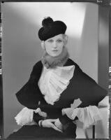 Peggy Hamilton modeling an Adrian gown with ruffles at the wrists and collar and a beret hat, 1933