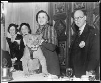 Peggy Hamilton, standing next to Ethel and Grace Bush, holds a lion cub at a Lions Club luncheon, Los Angeles, 1931-32