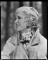 Peggy Hamilton modeling a coat with a wide collar and lapel, a hat and scarf, circa 1933