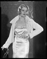 Actress (?) modeling a satin evening gown with jeweled sash and a fur jacket, circa 1931-1933