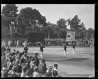 Two marching men carrying the banner announcing the Pasadena Elks marching band at the Tournament of Roses Parade, Pasadena, 1930