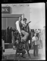 Couple on ladder on the sidewalk along the Rose Parade route, Pasadena, 1930