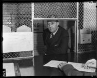 Clarence M. Fuller stands at the jail's booking counter, Los Angeles, between 1931-1934
