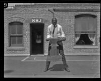 George Godfrey, heavyweight boxer, lifting an anvil [outside the KJH Radio studio, Los Angeles(?)], circa 1926-1927