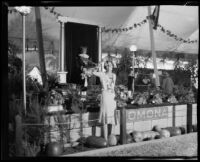 Woman poses in front of the Pomona agricultural exhibit at the Los Angeles County Fair, Pomona, 1930