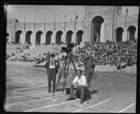 Newsmen beside a camera on a tripod during a Paavo Nurmi track event at the Coliseum, Los Angeles, 1925