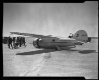 Small crowd gathers near Wiley Post's airplane, the Winnie Mae, Muroc Dry Lake, circa 1935