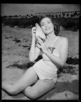 Betty Herrick [?] on beach with seashell, 1953-1964