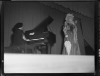 Lucille S. King, actress and ventriloquist, on stage singing, while other woman plays the piano, 1951