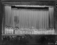 Children in costume lined up on a school auditorium stage, 1937