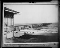 People at the beach next to a long wooden pier, Huntington Beach, original photograph 1908