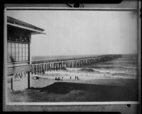 People at the beach next to a long wooden pier, Huntington Beach, original photograph 1908