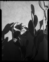 Mona Ohrtland standing against a wall behind a large prickly pear cactus, Palm Springs, 1940