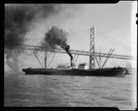 Cargo ship passing under the Bay Bridge, San Francisco, 1930s
