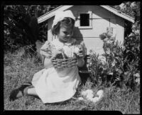Girl holding a basket seated outdoors next to a nest with eggs at the Children's Home Society, Los Angeles, 1935-1960