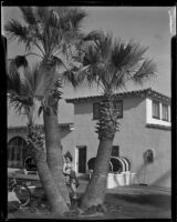 Carolyn Bartlett leaning against a palm tree outside of a building, Palm Springs, 1940