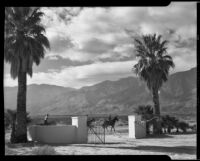 Horseback riders passing a gated drive on a dirt road, Palm Springs, 1941