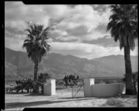 Wagon and stagecoach passing a gated drive on a dirt road, Palm Springs, 1941