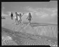 Three women running on a sand dune with one woman watching, Palm Springs vicinity, 1940-1941