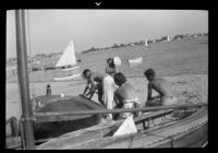 Beachgoers next to a boat on Balboa Peninsula with a view of Newport Bay, Newport Beach, 1937